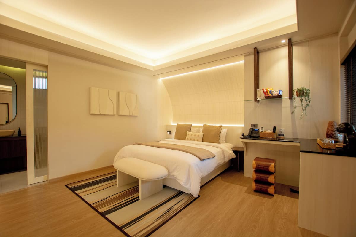 A modern bedroom with a large bed, bedside table, and a built-in desk with a chair.