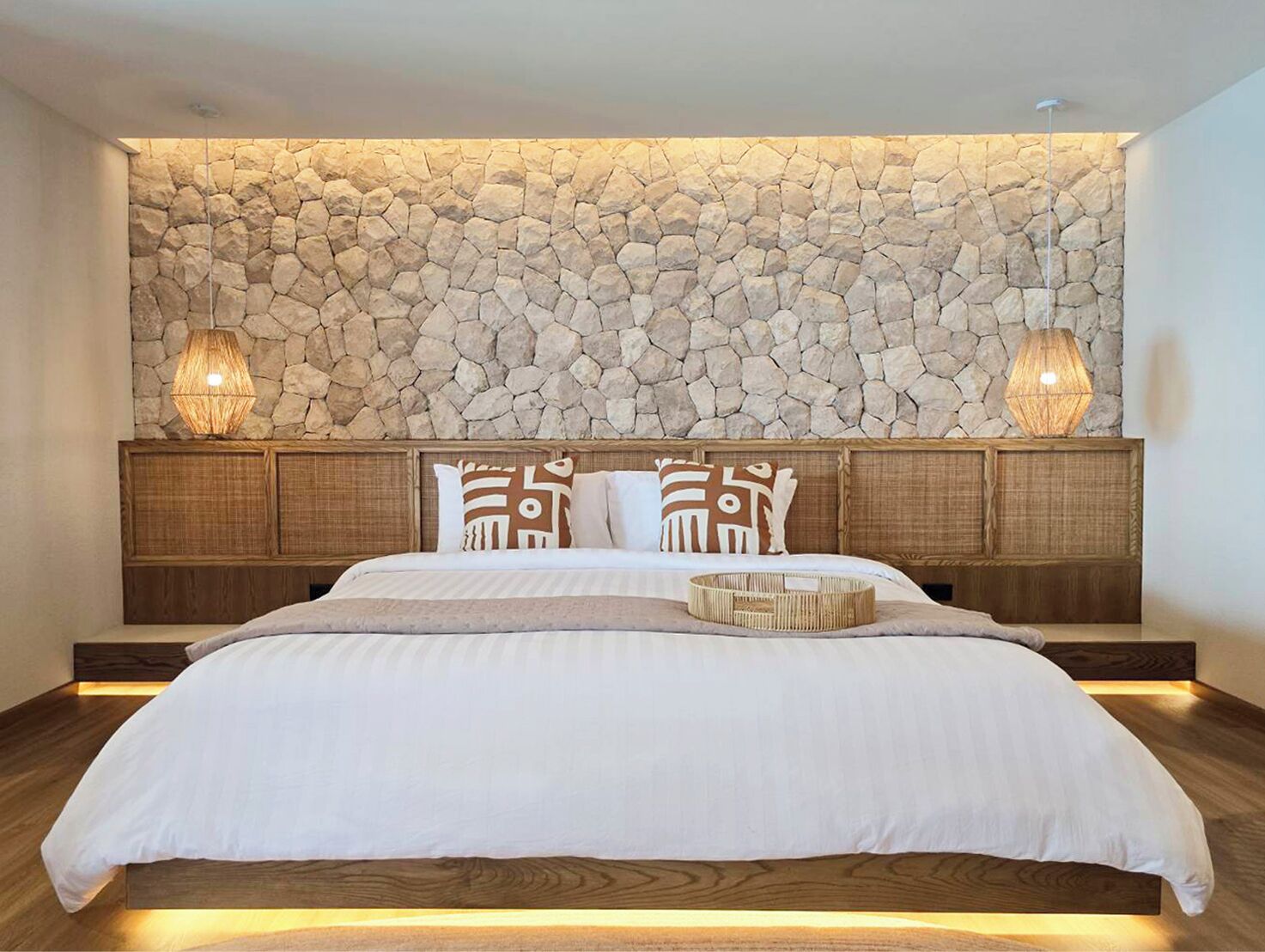 A bedroom with a stone wall, wooden headboard, and two bedside lamps.