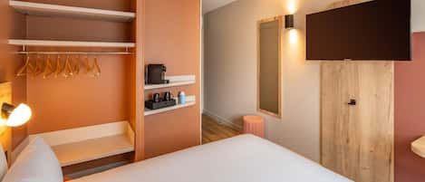 A hotel room with a bed, a wardrobe, a mirror, a television, and a shelf with toiletries.