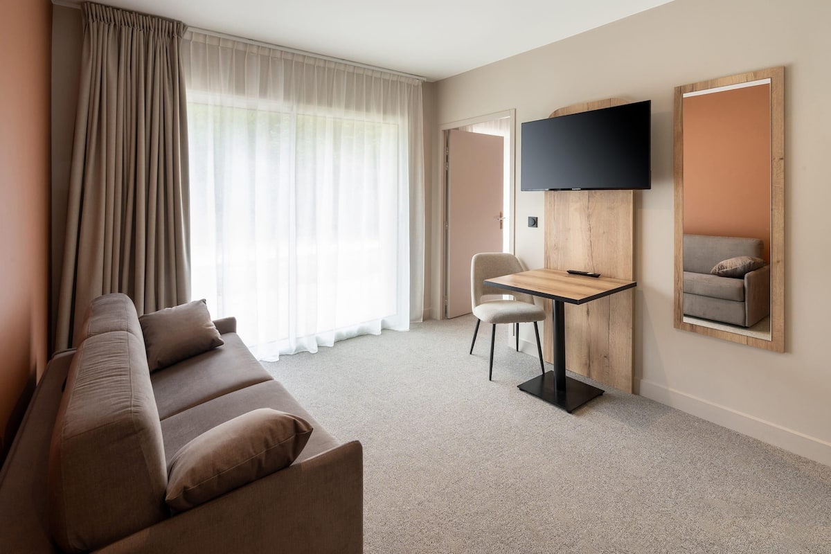 Quarto de hotel com sofá, escrivaninha, televisão e quadro na parede.