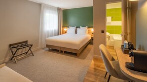 Hotelkamer met een bed, een bureau, een stoel, een kleine tafel en een badkamer zichtbaar door een open deur.