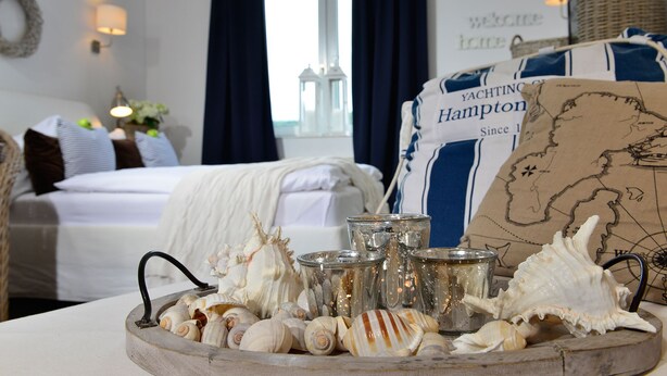 Een kamer met een bed, een tafel met zeeschelpen en glazen, en een kaart aan de muur.