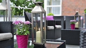 Een terras met rieten meubilair, een glazen tafel en een lantaarn met een kaars.