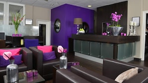 Een moderne lobby met donker leren banken, een paarse accentmuur en een receptiebalie met glazen pui.