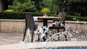 A pool area with a table and chairs, surrounded by a stone wall and greenery. - Hotel Grand Sal (Wieliczka)