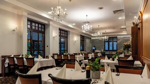 A dining area with tables set for guests, featuring chandeliers and a stone wall backdrop. - Hotel Grand Sal (Wieliczka)