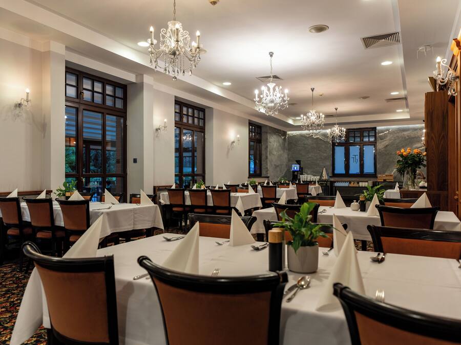 A dining area with tables set for guests, featuring chandeliers and a stone wall backdrop.
