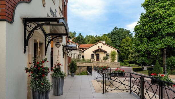 A hotel entrance with a covered walkway, potted plants, and a view of the surrounding buildings and greenery. - Hotel Grand Sal (Wieliczka)