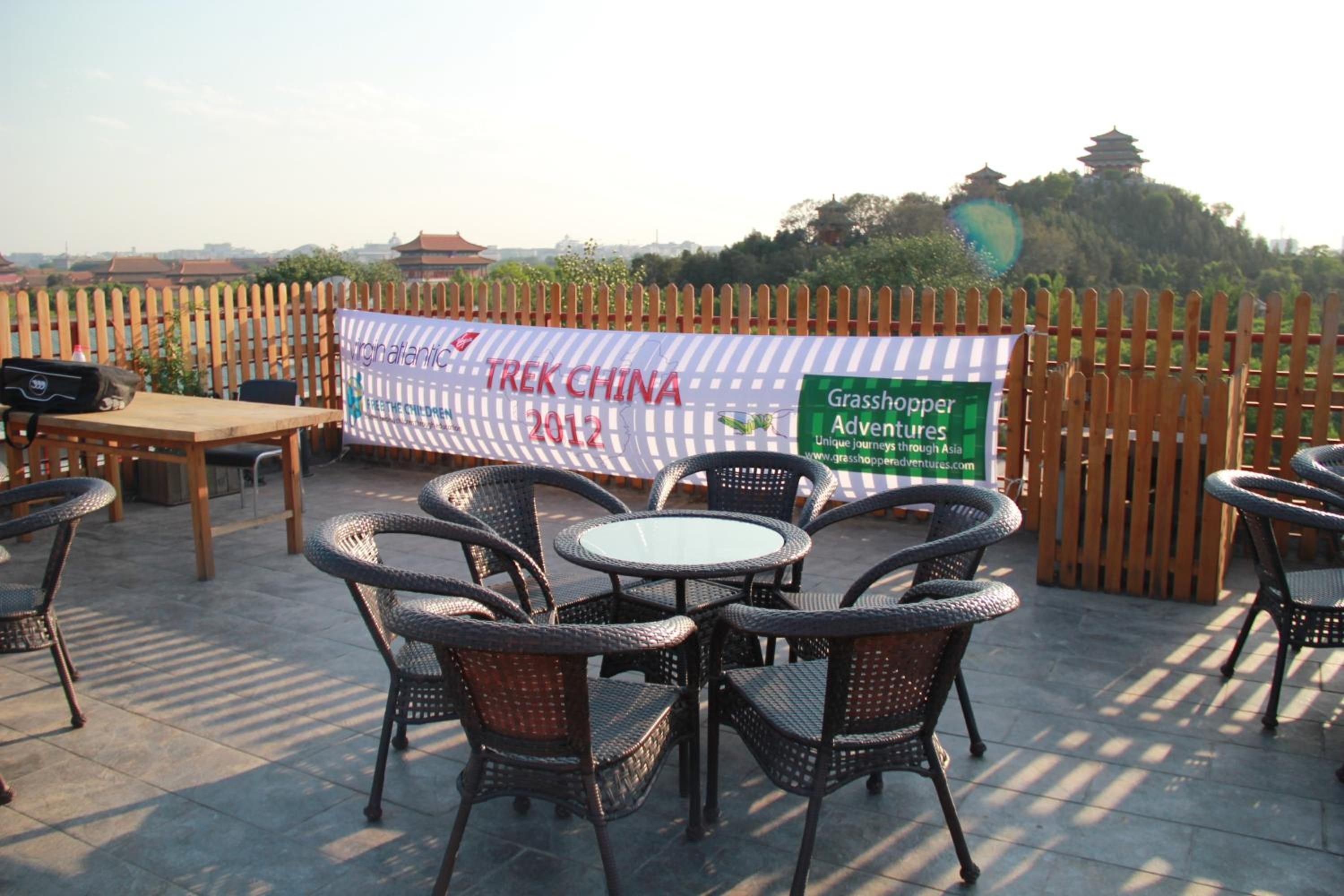 An outdoor seating area with wicker chairs and tables, a banner for 'Trek China 2012' and 'Grasshopper Adventures,' and a wooden fence in the background.