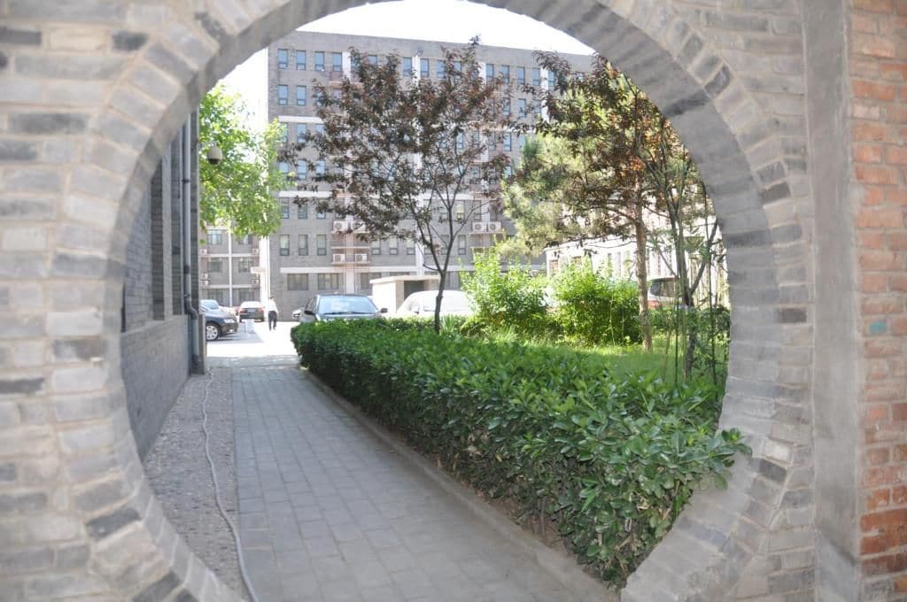 An arched stone structure with a paved walkway leading to a building with multiple windows.