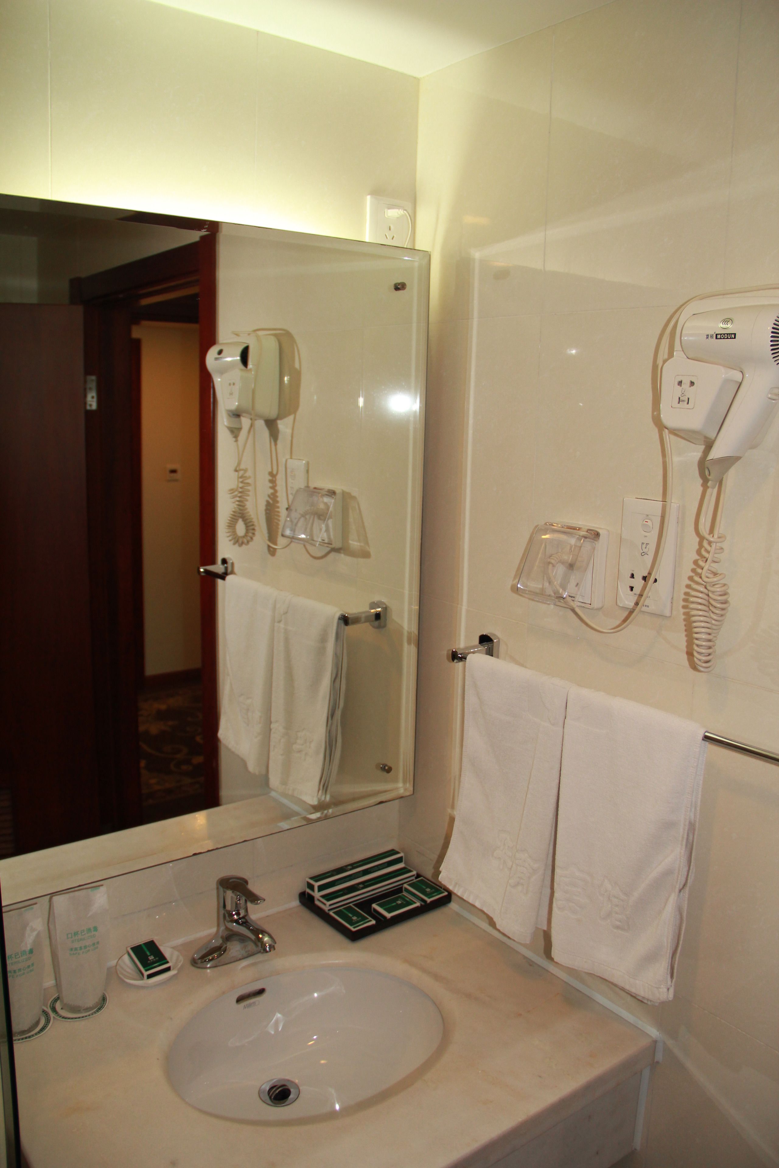 A hotel bathroom with a sink, mirror, towel rack, and hairdryer.