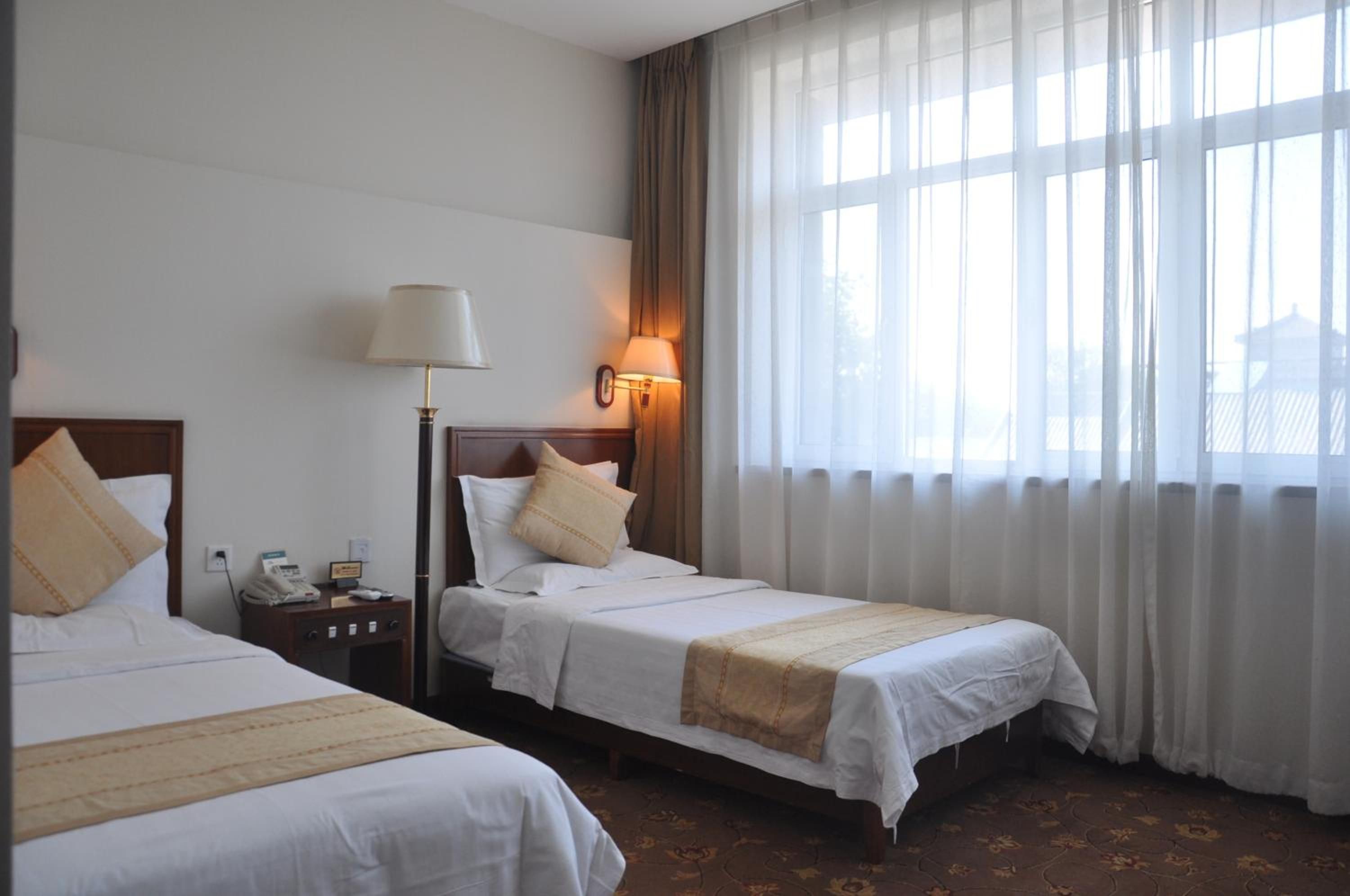 Une chambre d’hôtel avec deux lits, une table de chevet, une lampe et une fenêtre avec des rideaux.