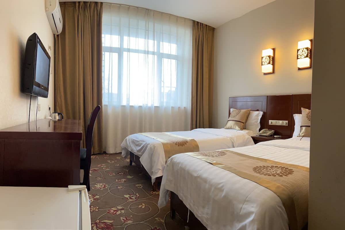 A hotel room with two beds, a desk, a television, and a window with curtains.