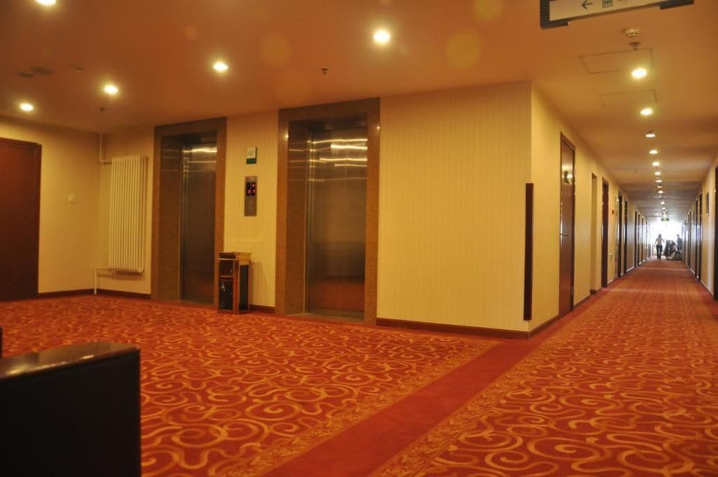 Corredor de hotel com piso em carpete, portas e elevador.