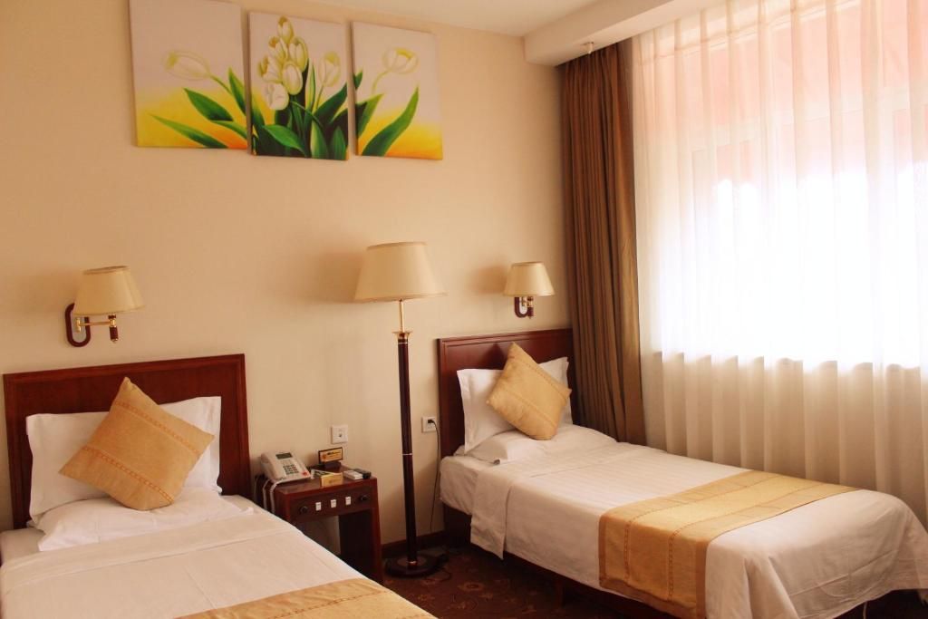 A hotel room with two beds, a bedside table with a lamp, a telephone, and artwork on the wall.