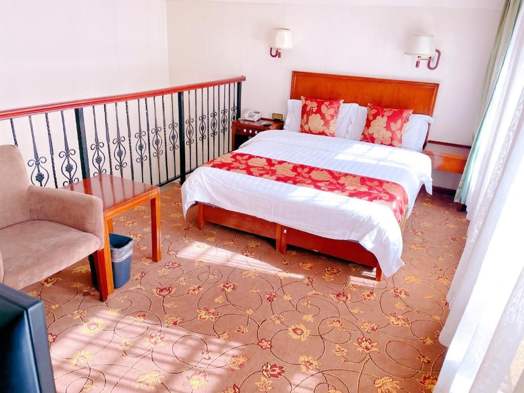 A hotel room with a bed, a chair, a nightstand, and a view of the outside.