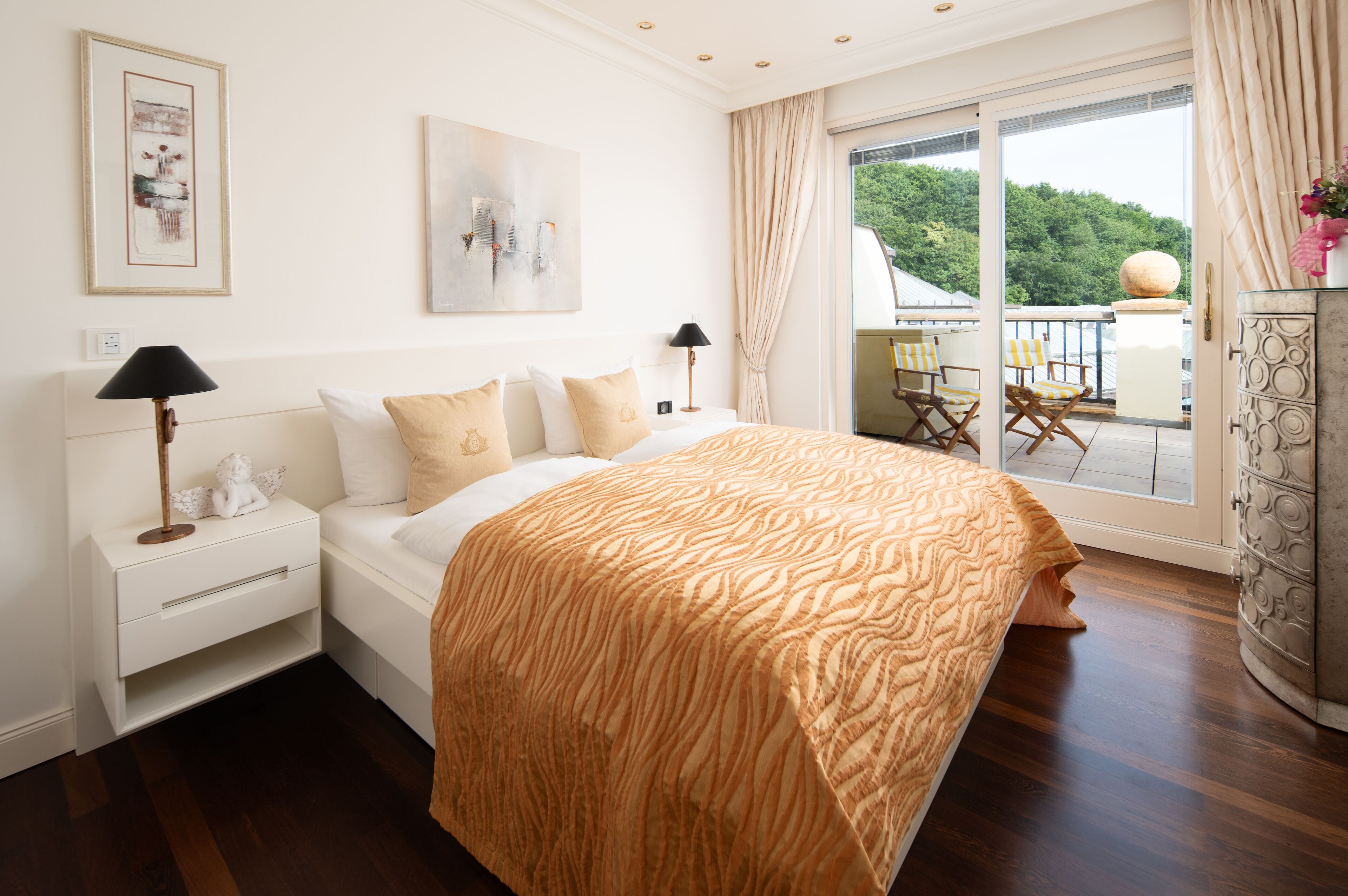 Ein Schlafzimmer mit einem großen Bett, einem Nachttisch, einer Lampe, einer Kommode und einem Balkon mit Sitzgelegenheiten.