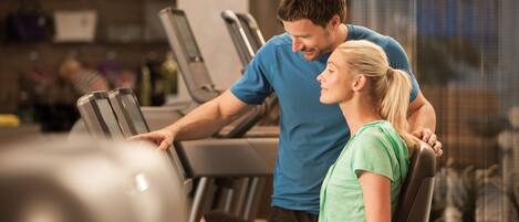 Un gimnasio con cintas de correr y una persona utilizándola.