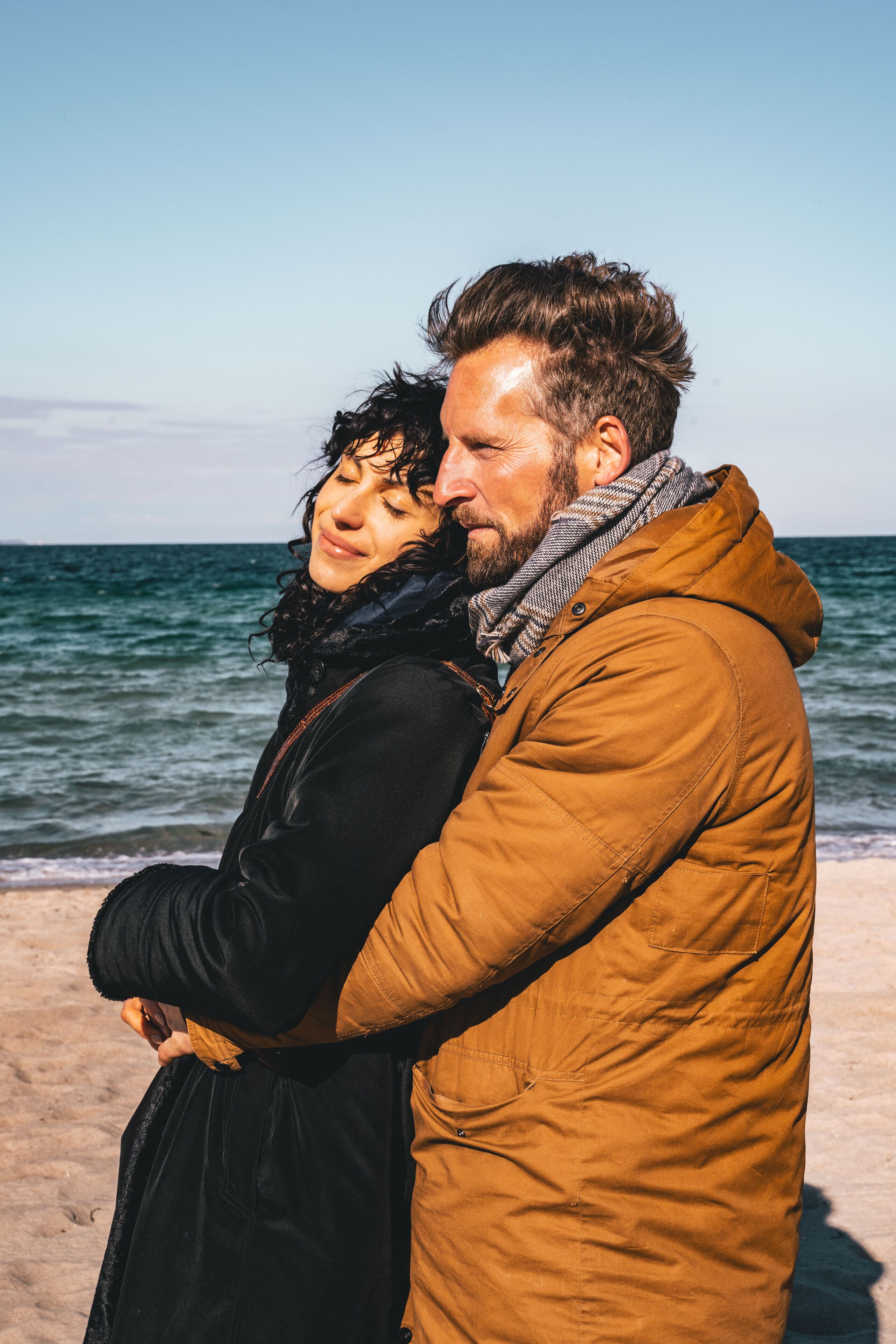 Una pareja abrazándose en la playa, con el océano al fondo.