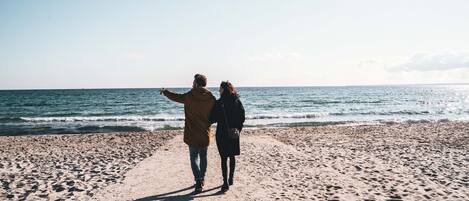 Two people walking on a sandy beach with the ocean in the background.