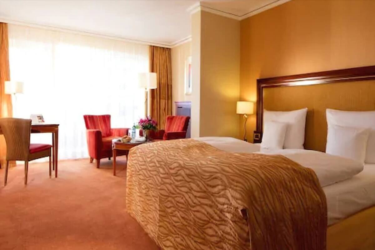 Quarto de hotel com uma cama grande, uma escrivaninha com cadeira e uma mesinha com um vaso de flores.