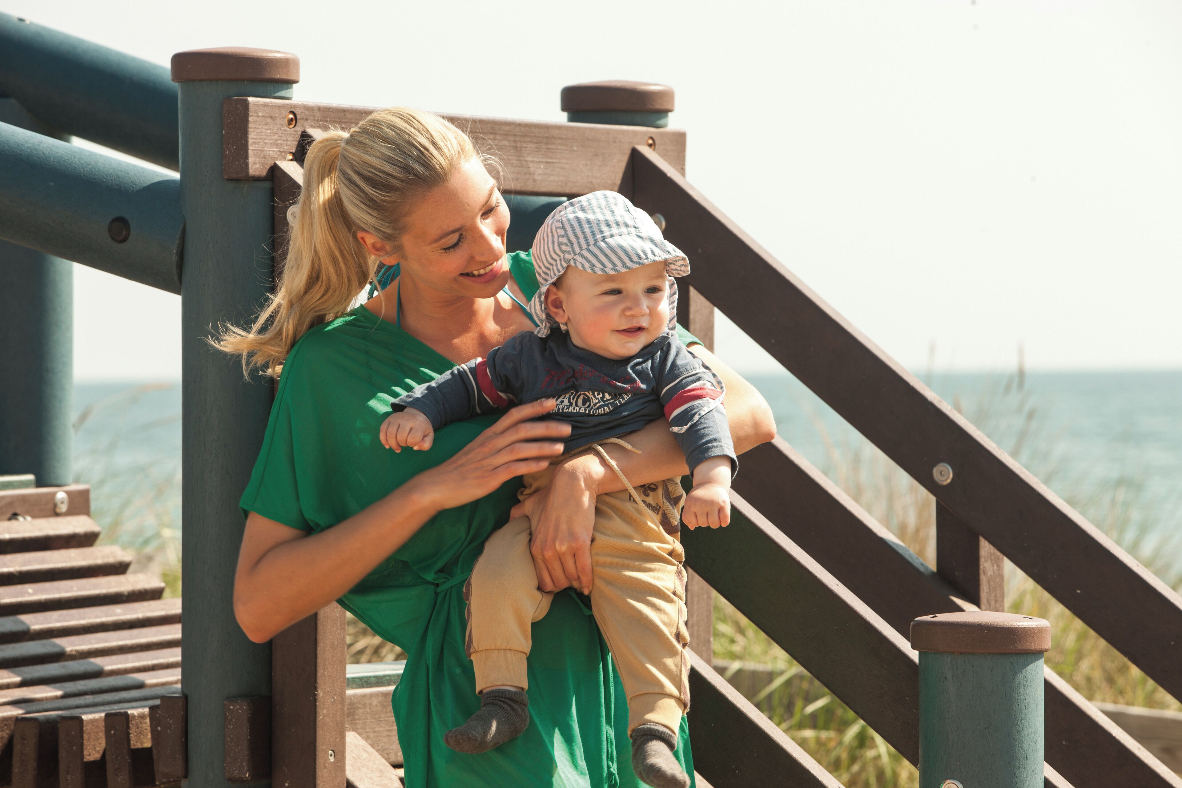 A person in a green shirt holding a child on a wooden staircase with a railing.