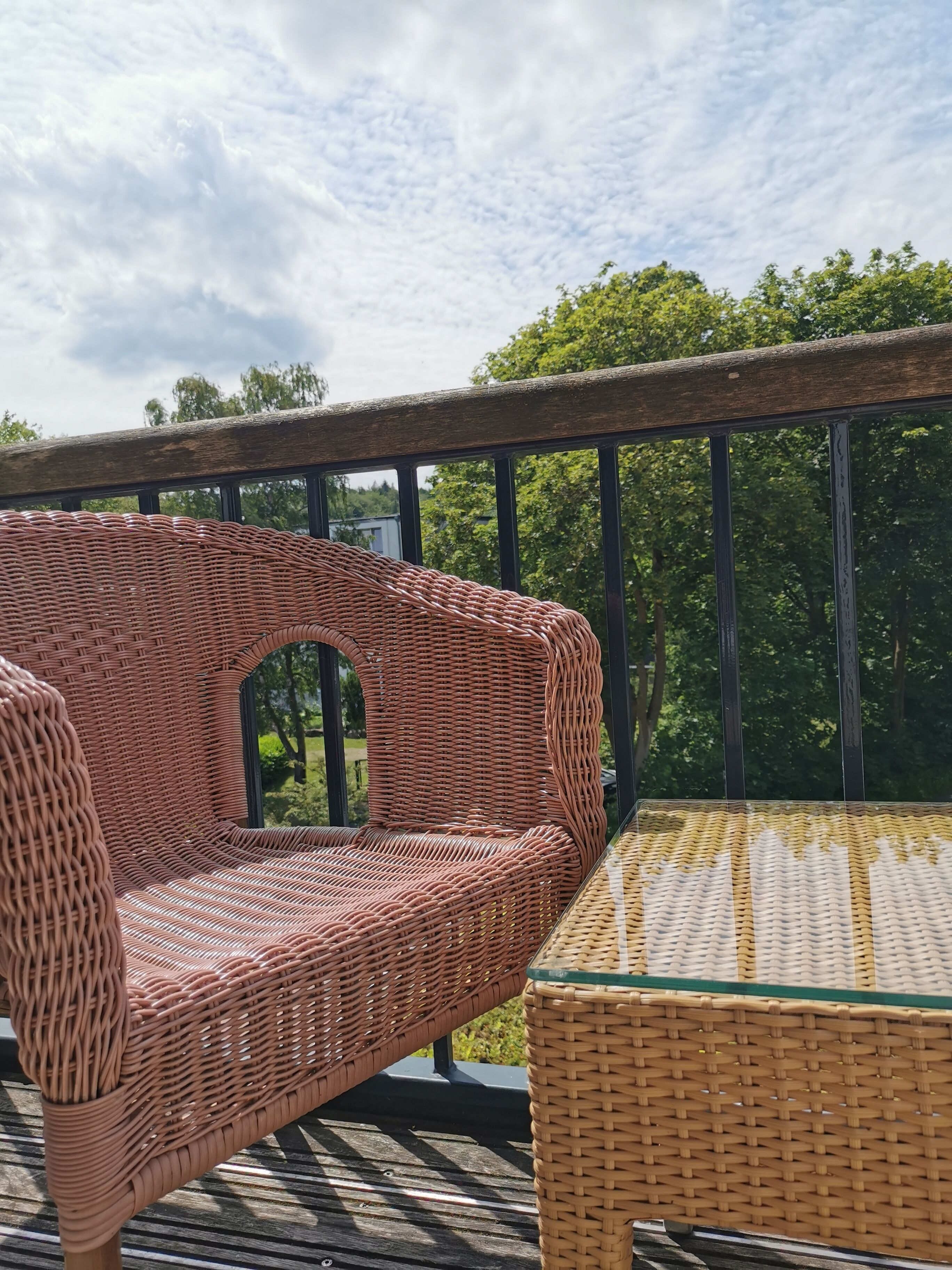 A wicker chair and table on an outdoor deck with a view of trees and a cloudy sky.