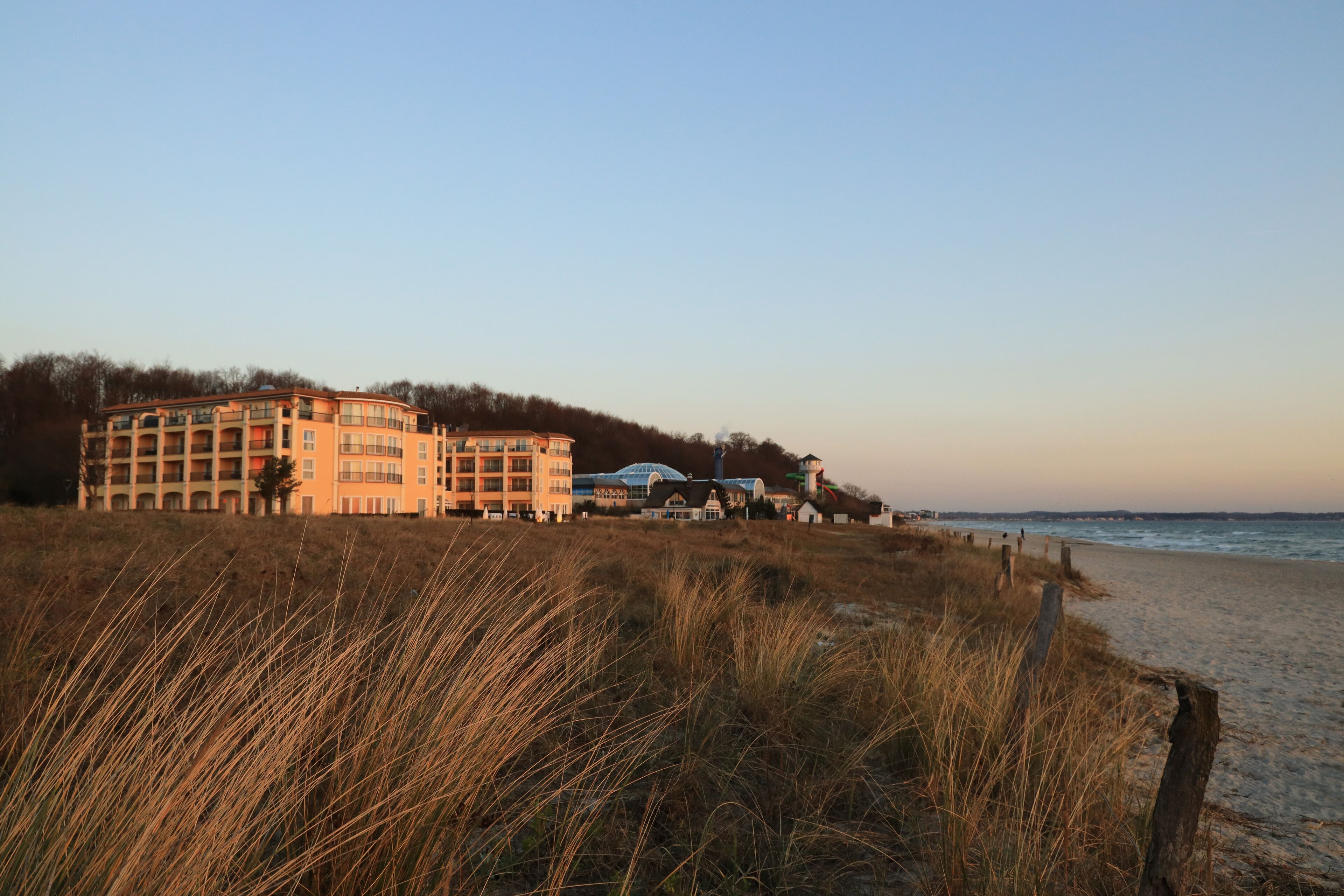 A beachfront hotel with multiple floors, a beach in the foreground, and a clear sky.