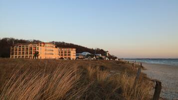 Un hotel frente a la playa con varios pisos, una playa en primer plano y un cielo despejado.