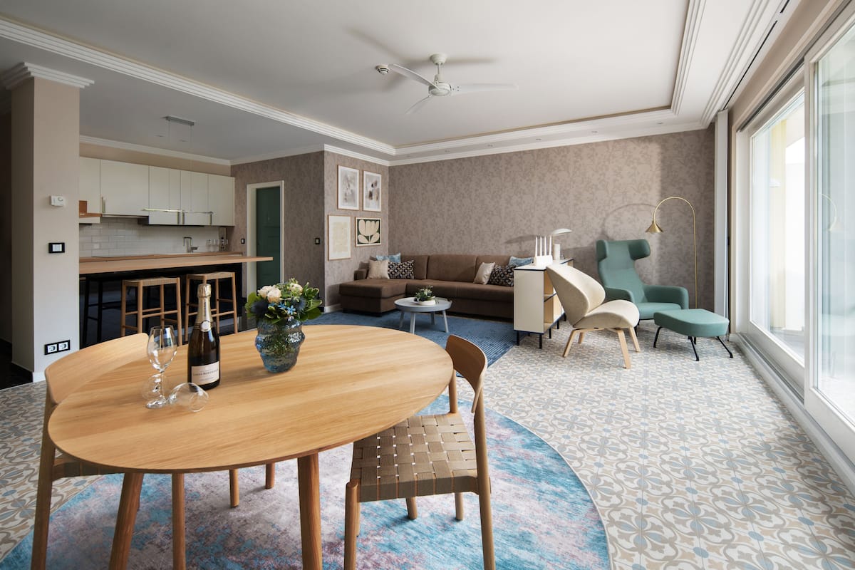 Quarto de hotel moderno com área de refeições, sofá, mesa pequena e uma janela grande.