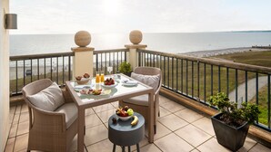 Un balcón con mobiliario de mimbre, una mesa dispuesta con frutas y bebidas, y vista al mar.