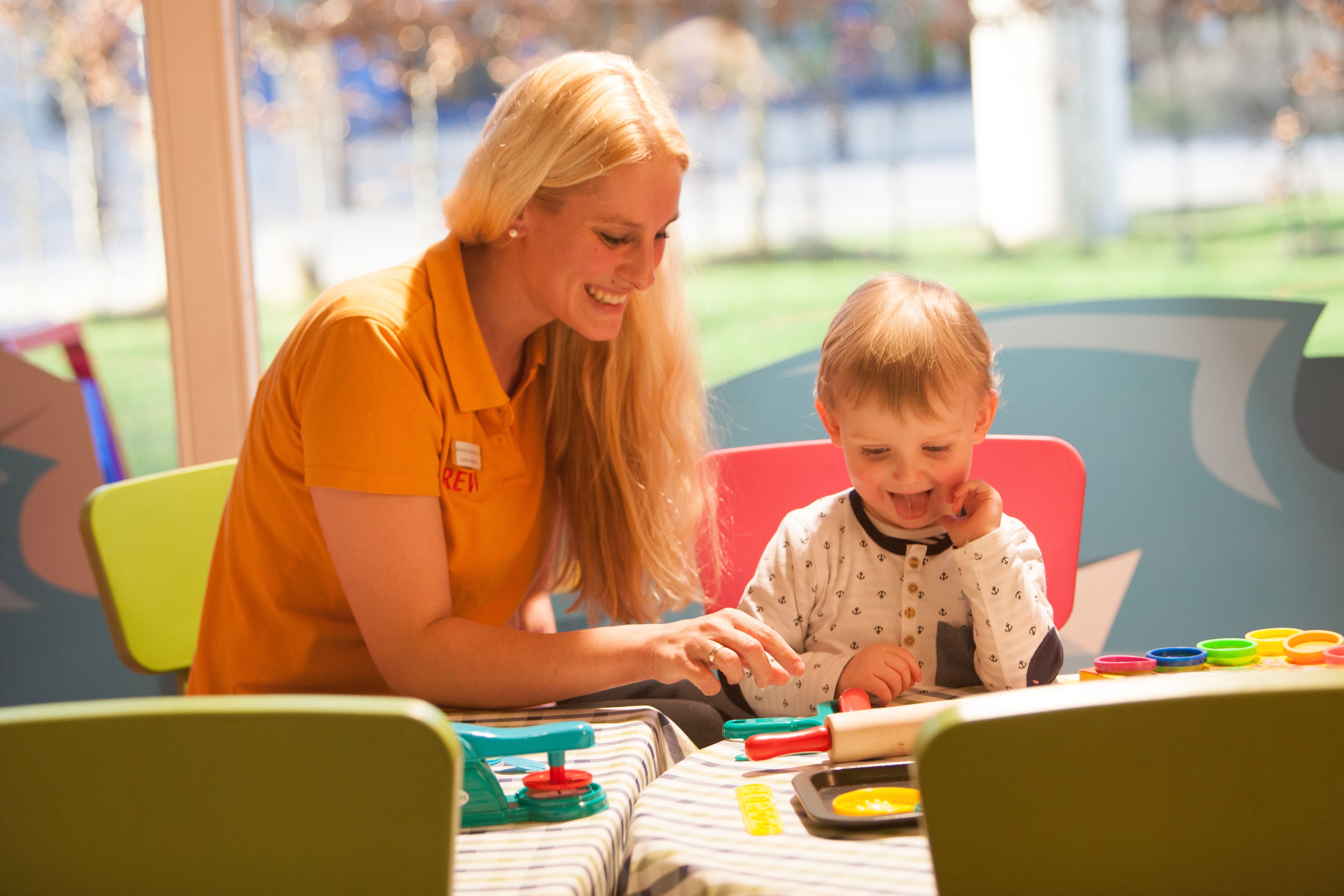 A woman and a child at a table with colorful toys and a striped tablecloth.