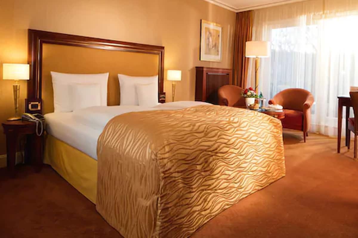 Quarto de hotel com uma cama grande, duas mesas de cabeceira, uma cadeira, uma escrivaninha e um abajur.