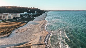Vista aérea de una playa con edificios y una colina arbolada al fondo.