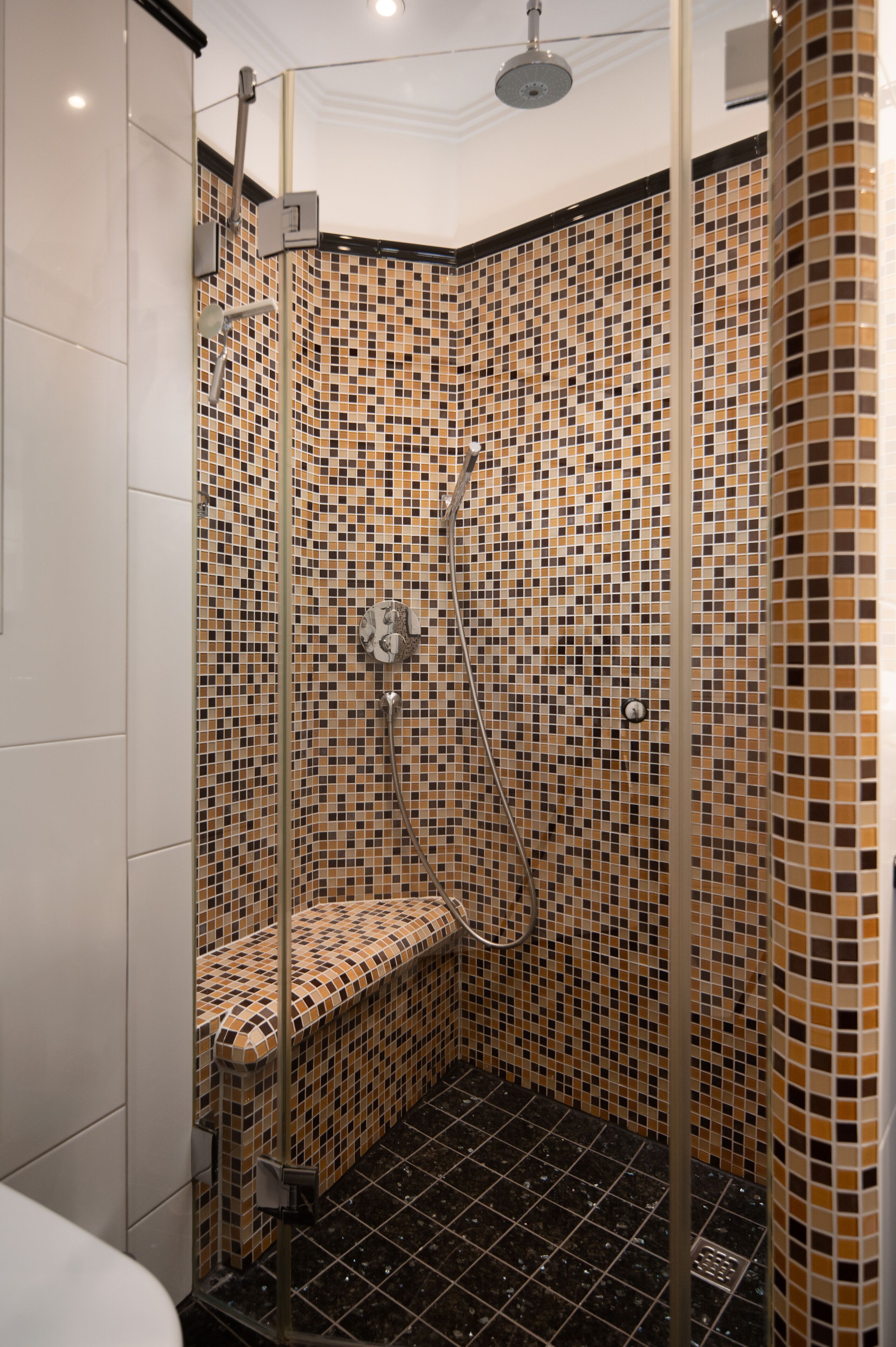Ducha con pared de mosaicos, banco y cabezal de ducha manual.