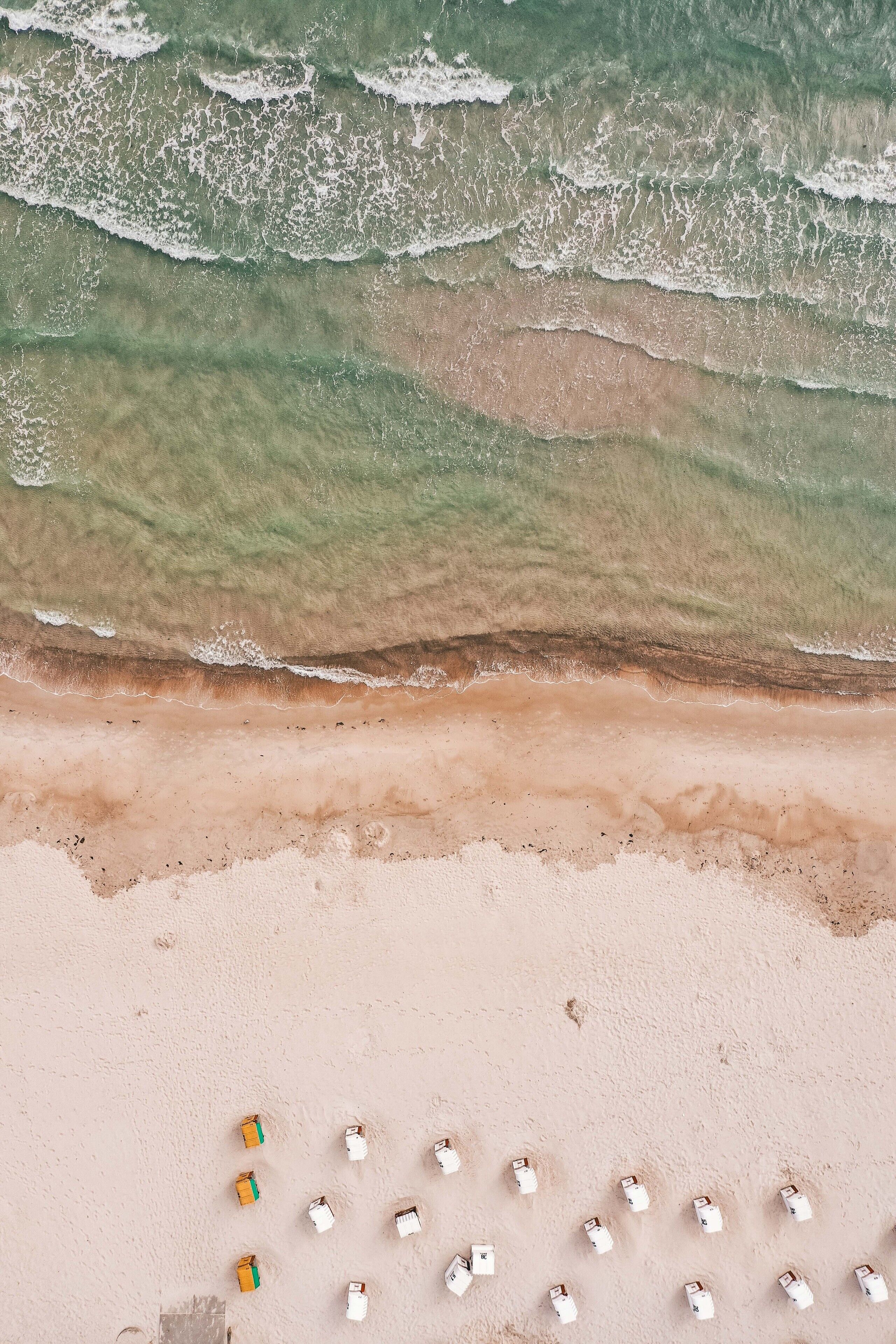 An aerial view of a beach with rows of beach chairs and umbrellas, a sandy shoreline, and waves approaching the shore.