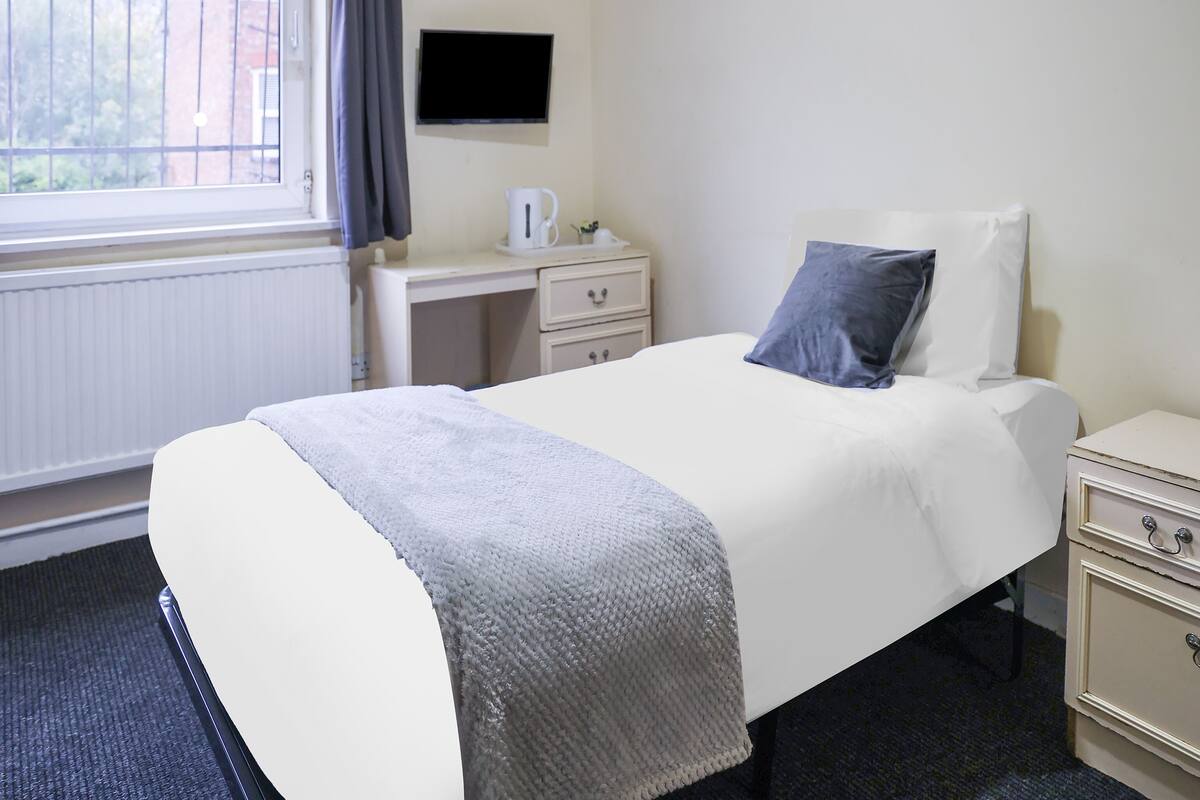 A hotel room with a bed, a desk, a chair, a TV, and a window with curtains.