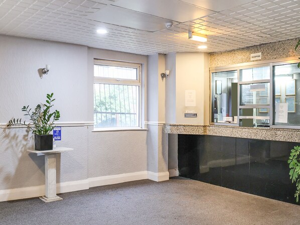 A reception area with a reception desk, a potted plant, a window, and a wall-mounted sign.
