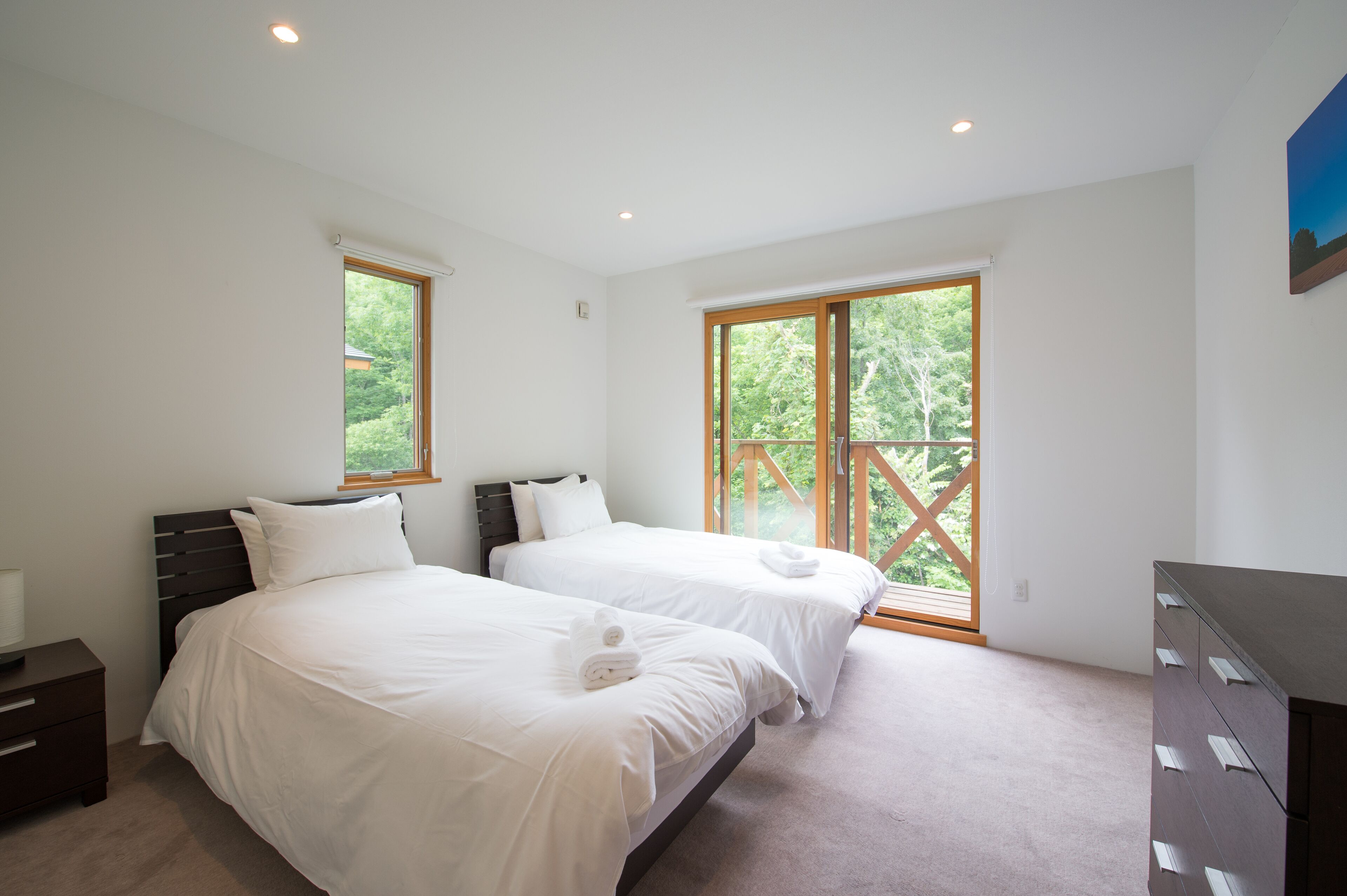 Un dormitorio con dos camas, un aparador y una ventana con vistas a zonas verdes.