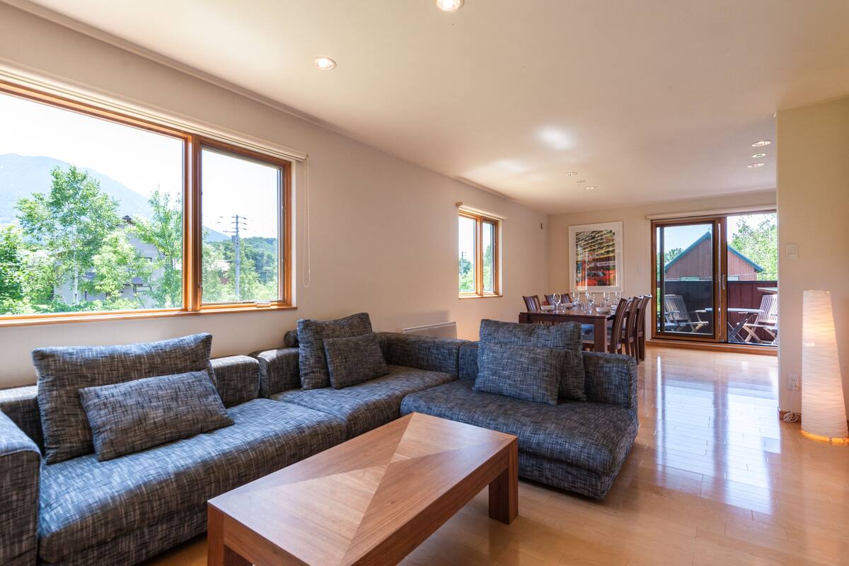 A modern living room with a large sectional sofa, a wooden coffee table, and a dining area with a table and chairs.