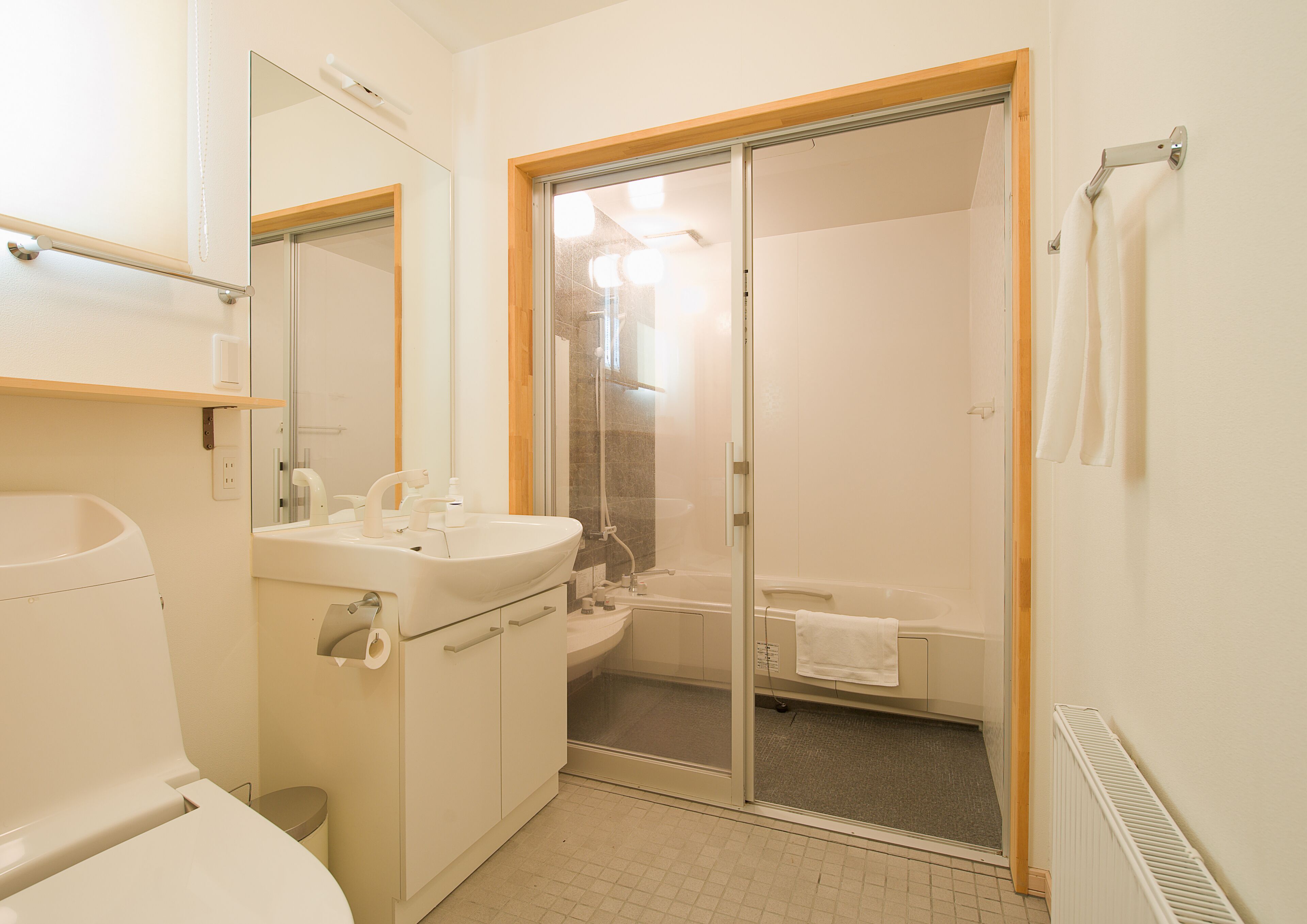 A bathroom with a toilet, sink, mirror, and a glass-enclosed shower area.