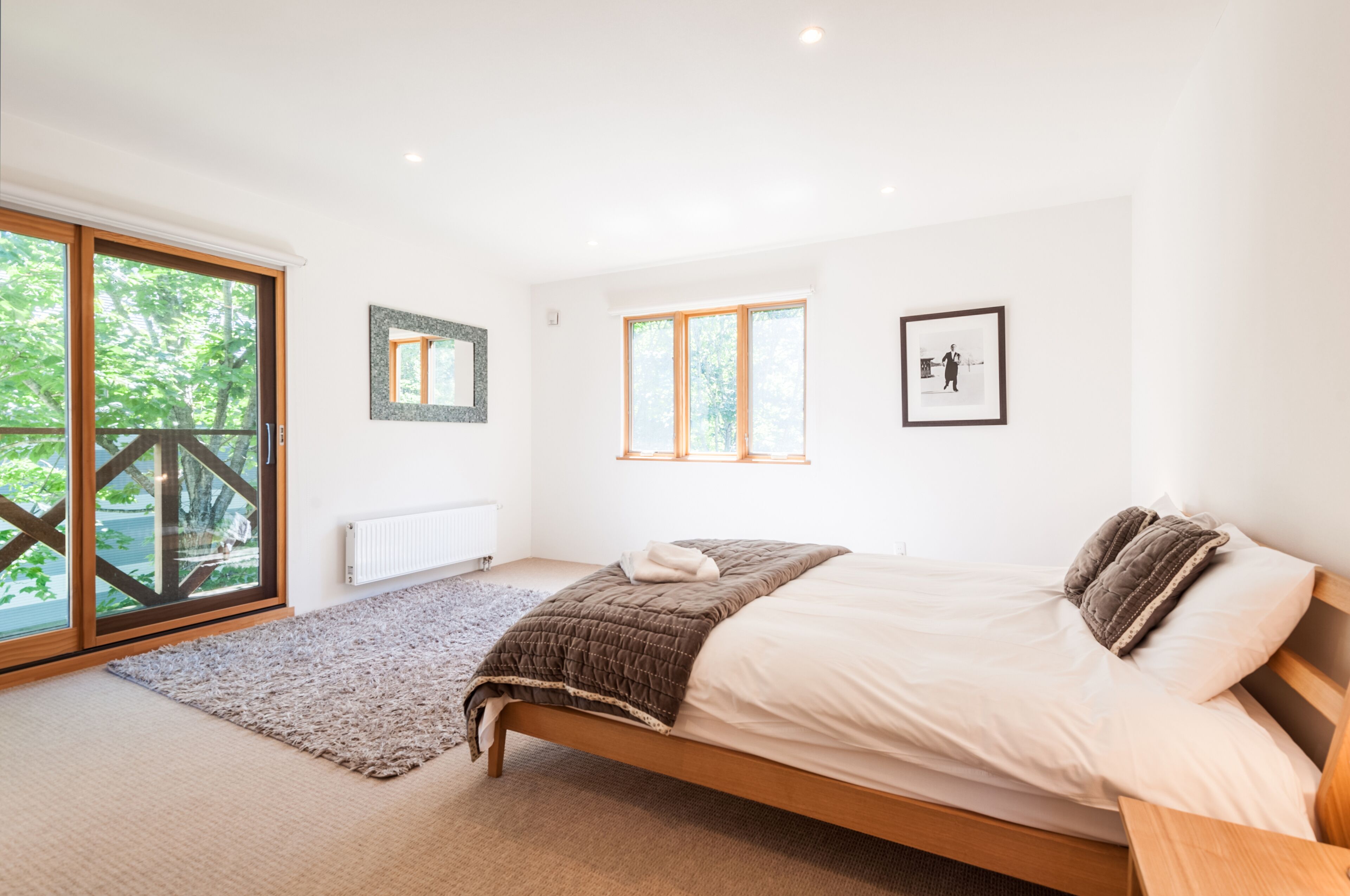 A bedroom with a bed, a large window, and a view of greenery outside.