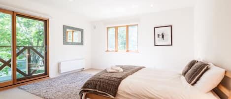 A bedroom with a bed, a large window, and a view of greenery outside.