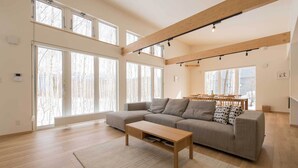 A spacious living room with a large sectional sofa, a wooden coffee table, and a dining area with a table and chairs. - Country Resort Niseko (Kutchan)