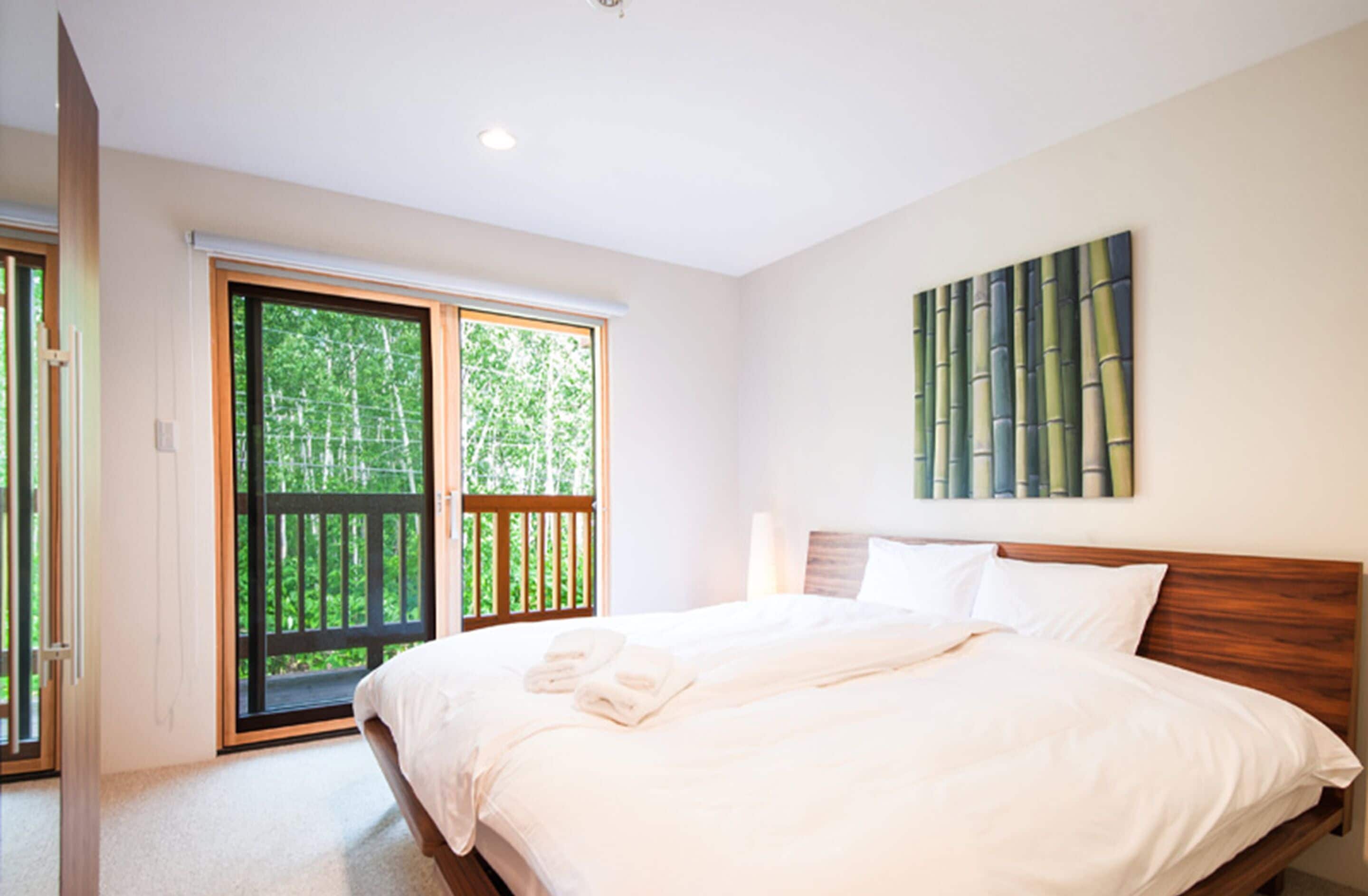 A bedroom with a large bed, a sliding glass door to a balcony, and a wall-mounted artwork.