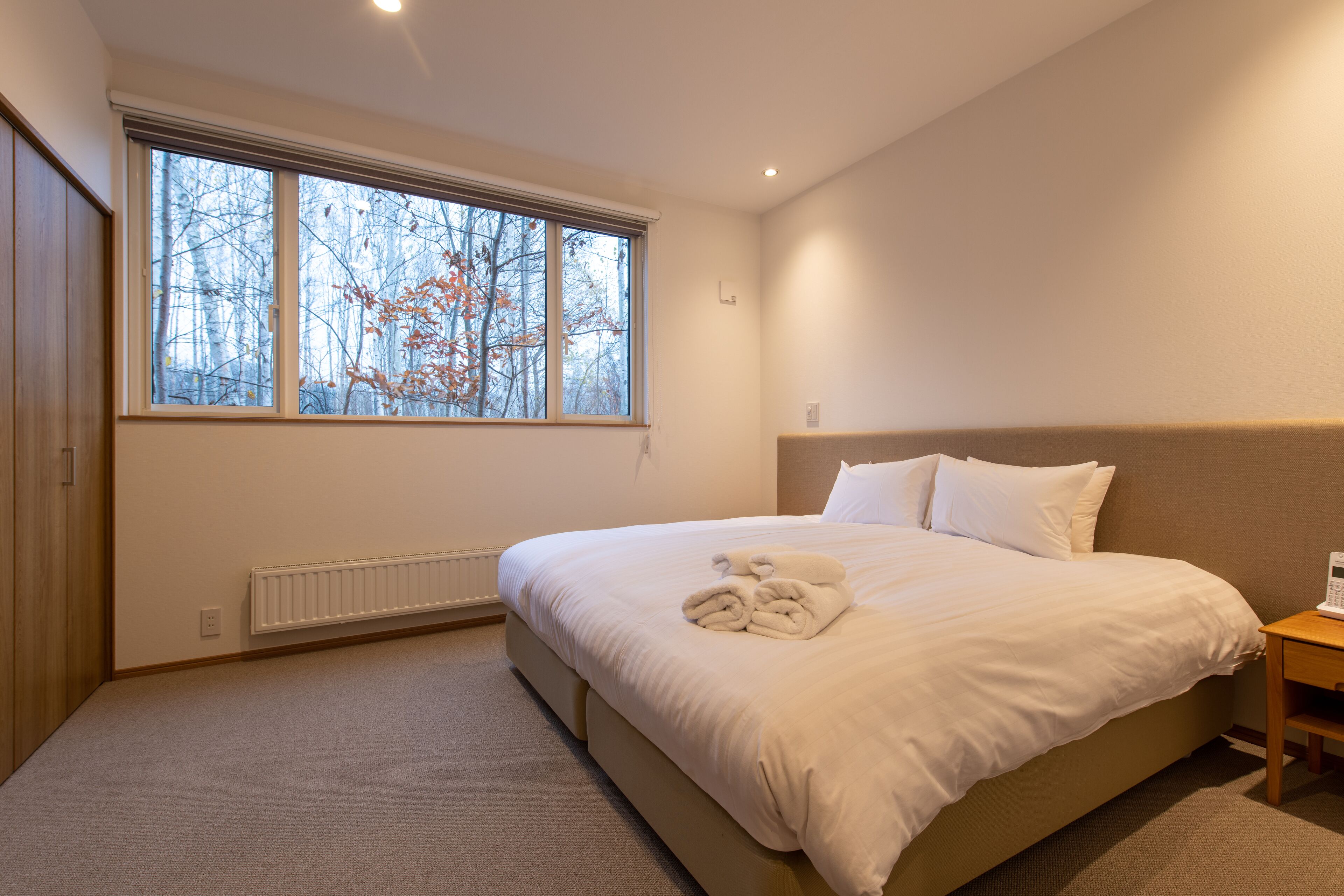 Ein Schlafzimmer mit großem Fenster, einem Bett, einem Nachttisch und einer Heizung.
