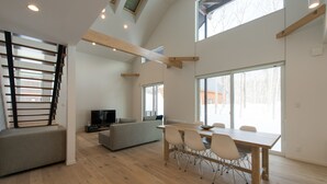 A spacious living area with a dining table, sofa, and TV. - Country Resort Niseko (Kutchan)