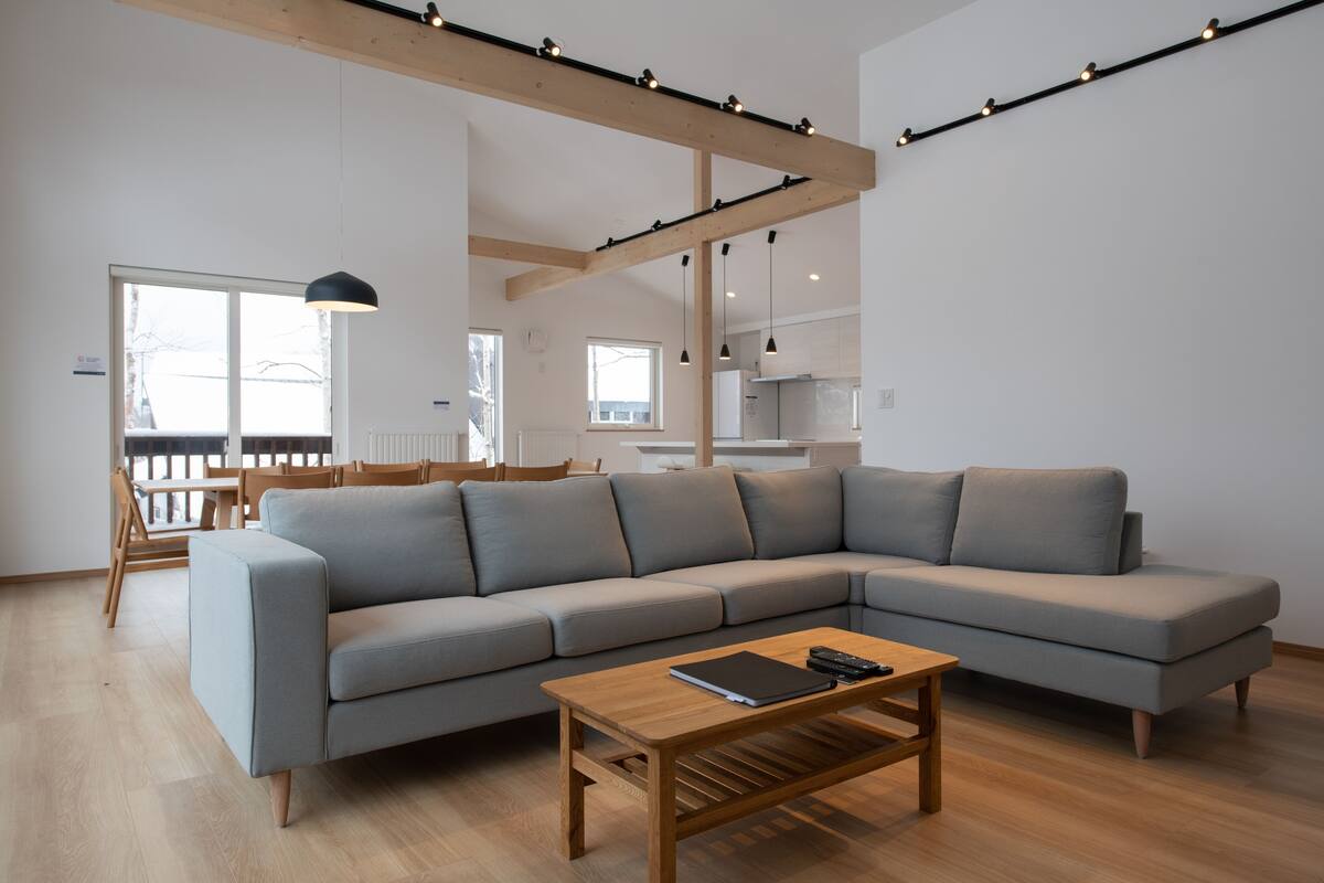 A modern living room with a grey sectional sofa, a wooden coffee table, and a dining area with wooden chairs and a table.