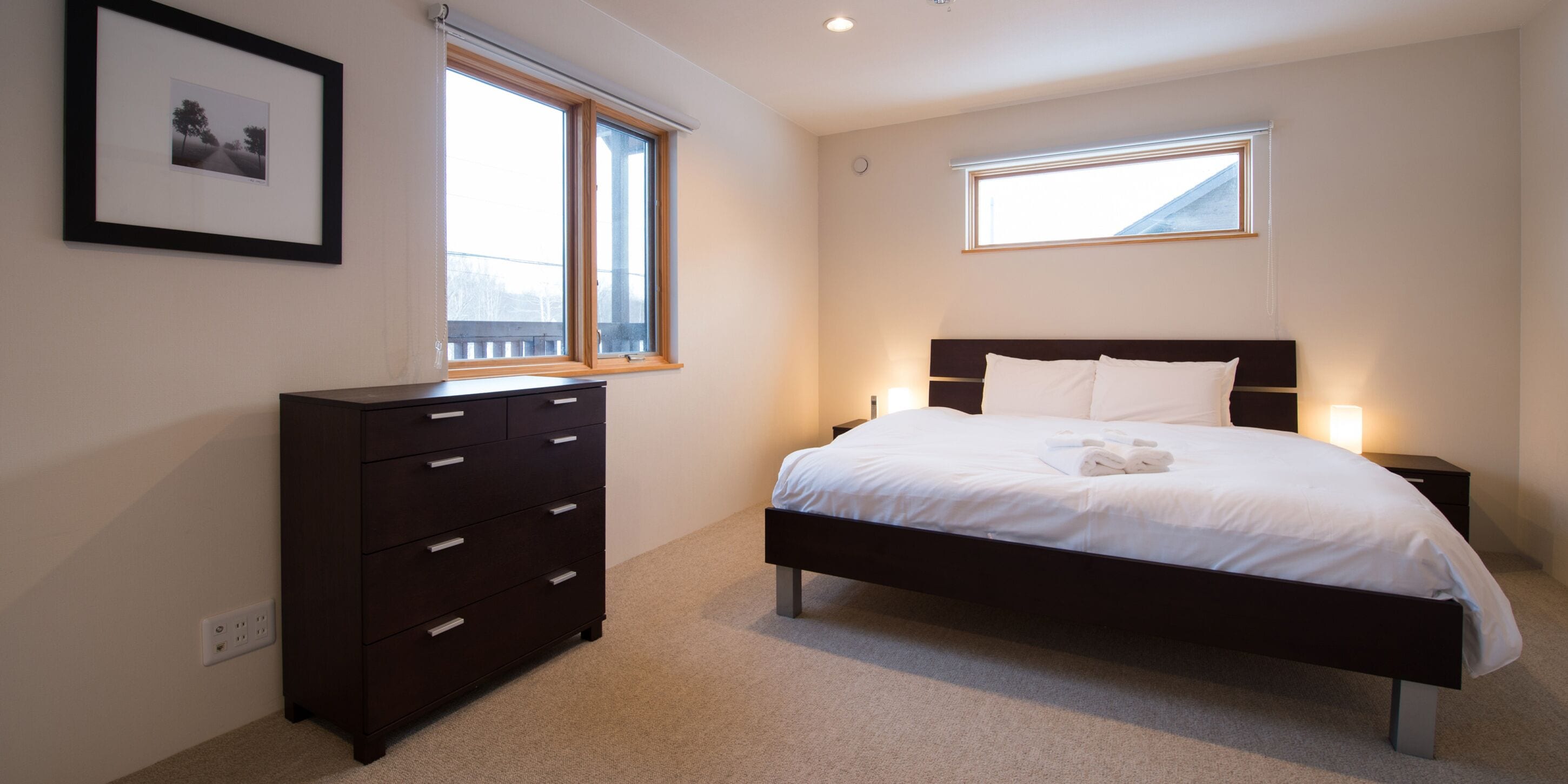 A bedroom with a bed, a dresser, two windows, and a framed picture on the wall.
