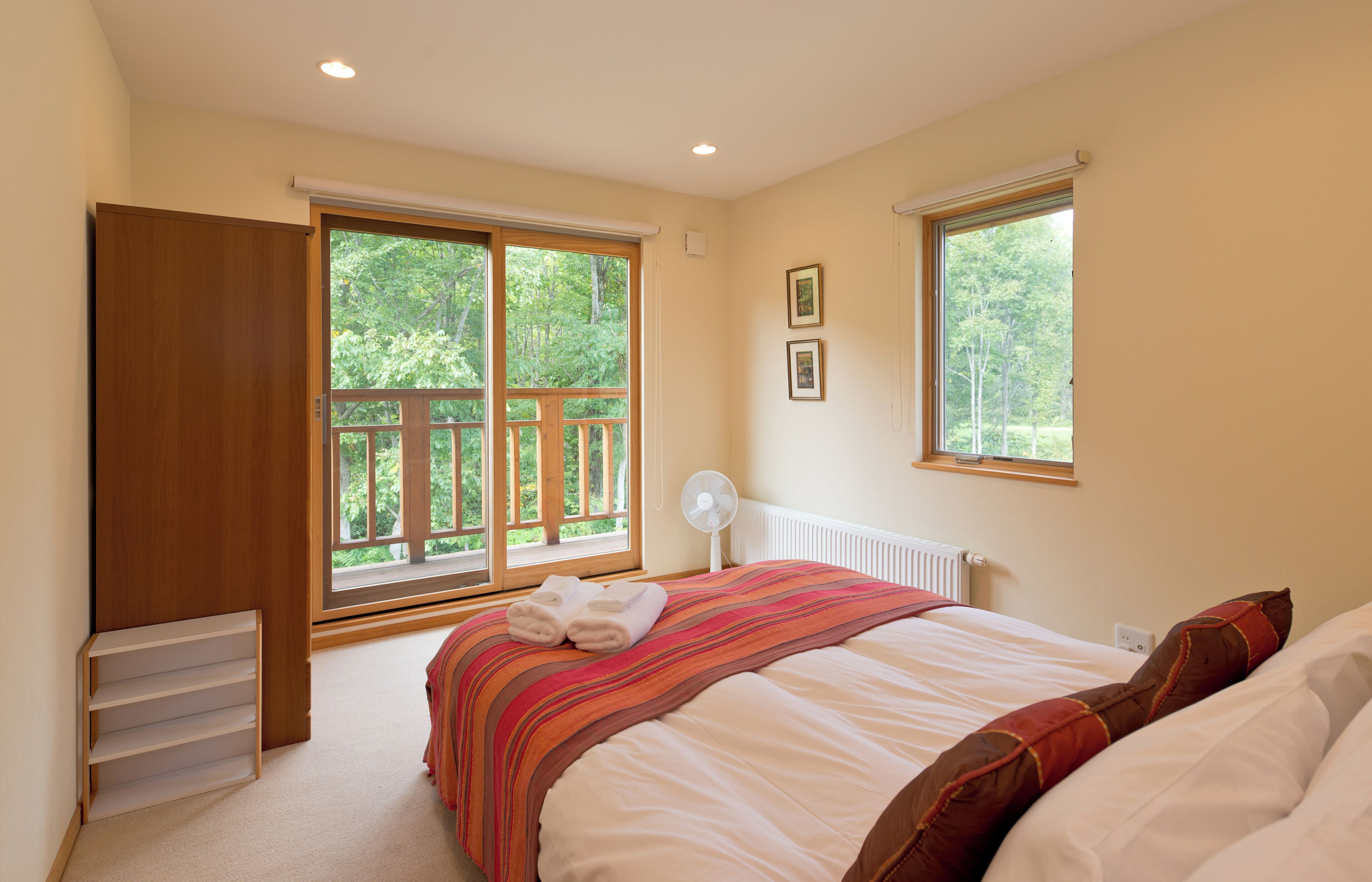 A bedroom with a bed, a window, a radiator, and a fan.